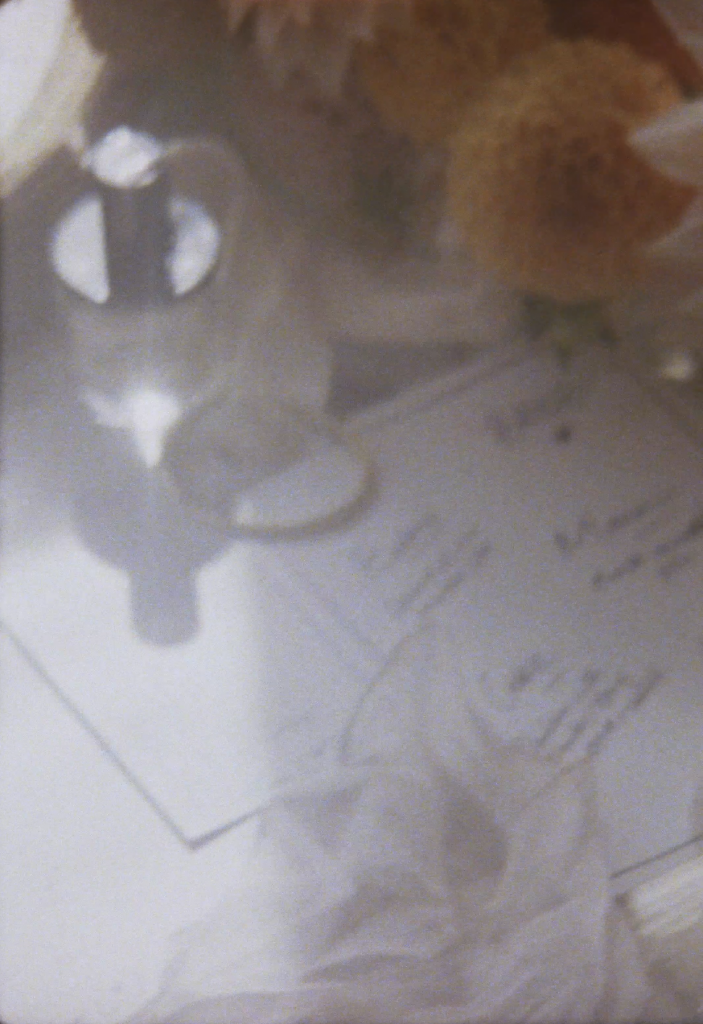 Still frame from a super 8 film footage showing wedding flowers, perfume and invites