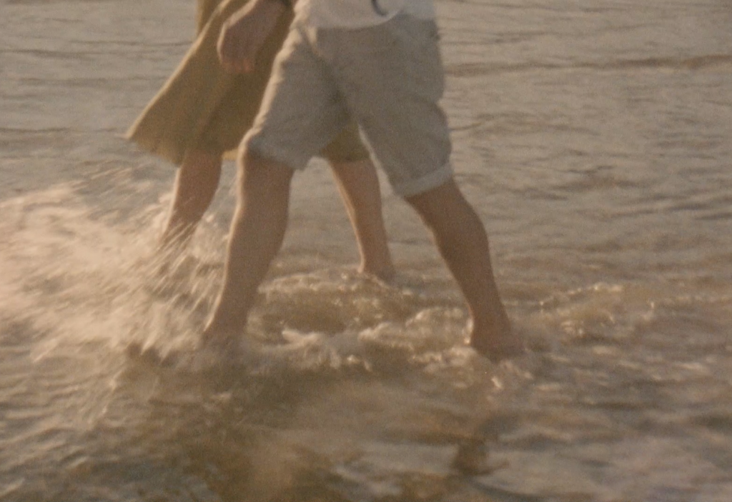 Still frame from a super 8 film footage showing a couple walking in the water at the beach
