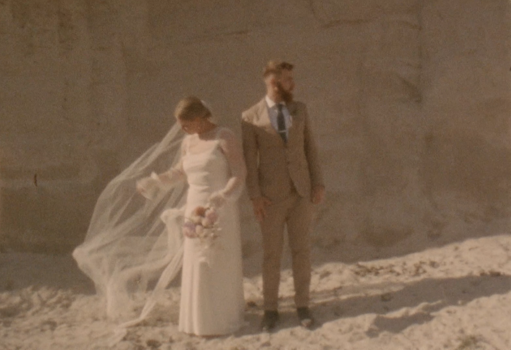 Still frame from a super 8 film footage showing a bride and groom in front of a natural white clay cliff