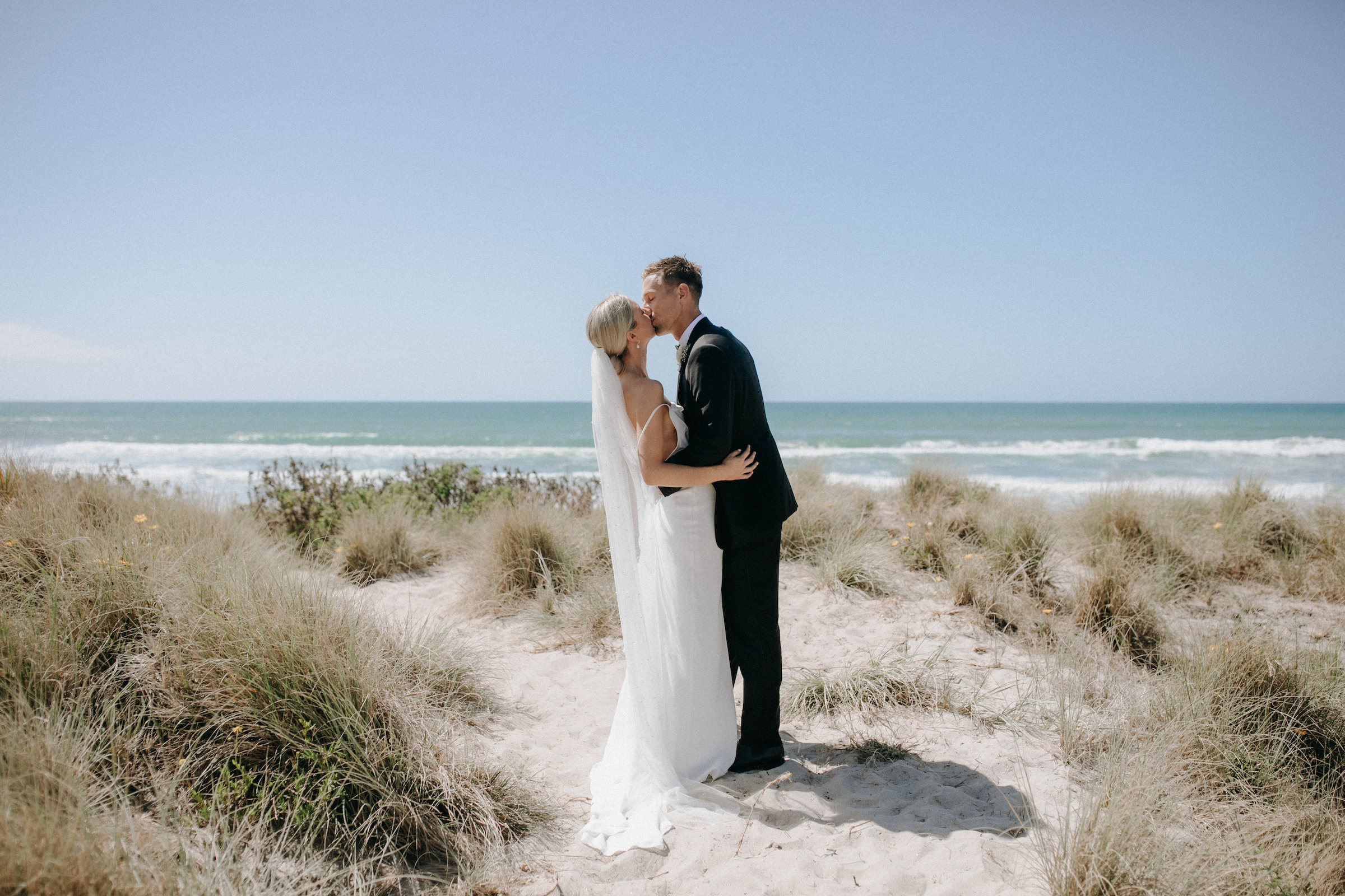 bride and groom kissing in the middle of the wonders of 99 palms with beach view and tall grass