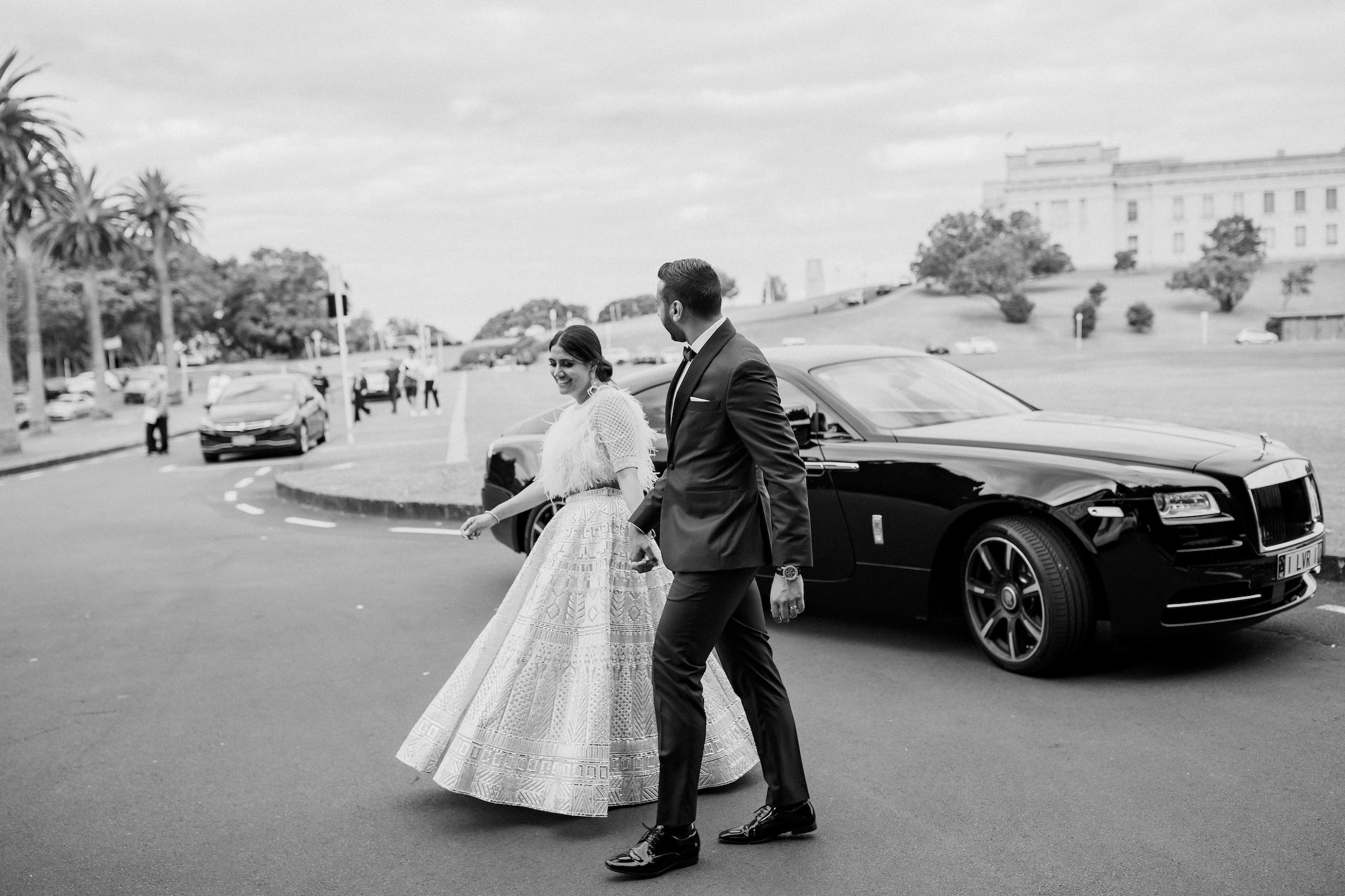 Bride wearing traditional indian dress and groom wearing tuxedo walking hand and hand as they get out of a black Rolls Royce Auckland Wedding Ana Galloway Photography