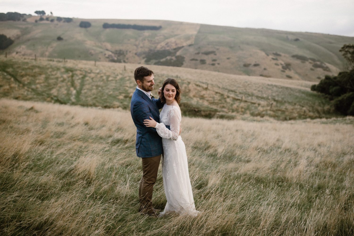 Elegant bride and groom embracing each other in a field of grass, bride wears a vintage lace gown Dunedin weddings - Ana Galloway Photography